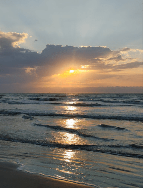 Sunset over the ocean, with rays of light breaking through clouds and reflecting on the water's surface.