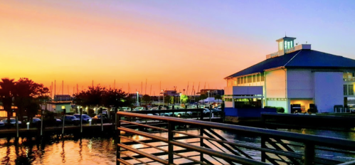 A vibrant sunset over a marina, with boats and a modern building reflecting the colorful sky.
