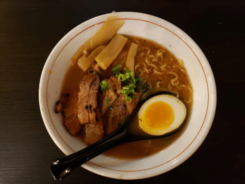 A bowl of ramen with sliced pork, bamboo shoots, green onions, and a soft-boiled egg in rich broth.