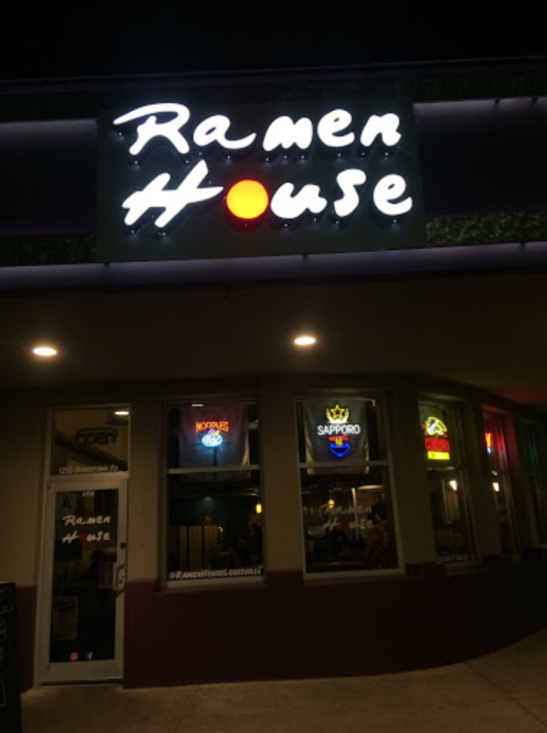 A nighttime view of Ramen House, featuring a bright sign and illuminated windows with various beer logos.