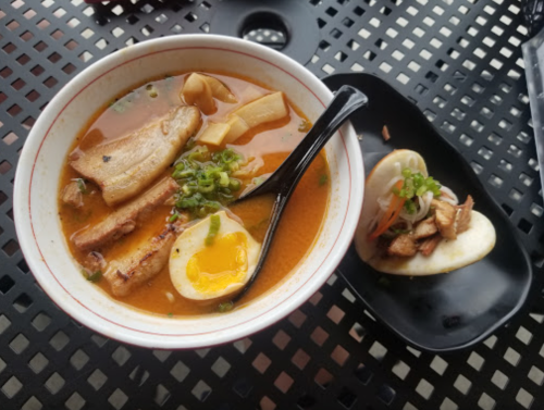 A bowl of ramen with pork, egg, and green onions, alongside a plate of bao with pulled pork and vegetables.