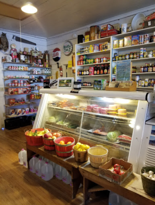 A cozy store interior featuring a refrigerated display, baskets of fruit, and shelves stocked with various goods.
