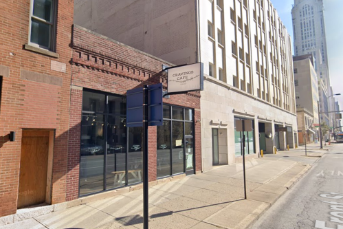Exterior of Cravings Café on a city street, featuring large windows and a sign, with buildings in the background.