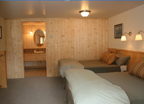 Cozy bedroom with two twin beds, wooden walls, and a bathroom visible through an open door.