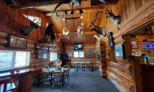 Cozy log cabin interior with mounted animal heads, wooden furniture, and a TV, creating a rustic dining atmosphere.