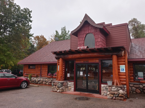 A rustic log cabin-style building with a red roof and stone accents, surrounded by trees on a cloudy day.