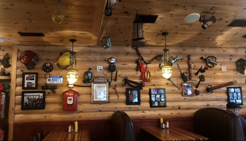 A rustic restaurant interior featuring a wooden wall adorned with vintage firefighting equipment and framed photos.