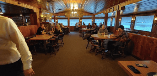A cozy restaurant interior with wooden decor, tables occupied by diners, and a warm, inviting atmosphere.