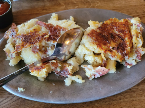 A plate of crispy potato pancakes with bits of bacon, served with a spoon on a wooden table.