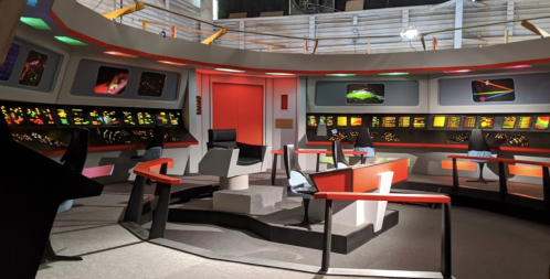 Interior of a futuristic spaceship bridge with colorful control panels and seating, reminiscent of classic sci-fi.
