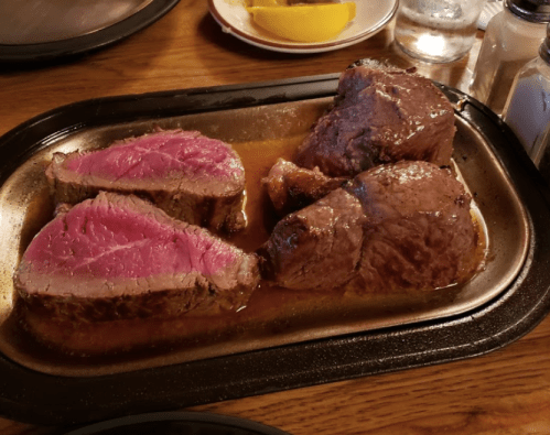 A sizzling platter of medium-rare beef, sliced and resting in savory juices, served on a wooden table.