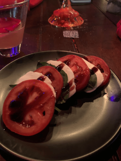 A plate with slices of tomato and mozzarella cheese, layered with basil and drizzled with balsamic glaze.