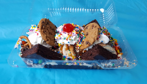 A colorful dessert platter with brownies, cookies, ice cream, whipped cream, sprinkles, and a cherry on top.