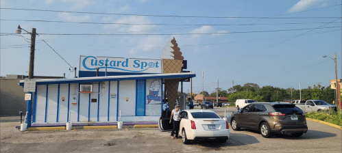 A small ice cream shop named "Custard Spot" with cars parked outside on a sunny day.