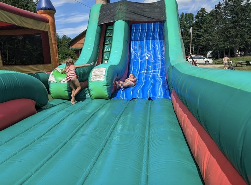 A child slides down a colorful inflatable slide while another child runs up beside them on a sunny day.