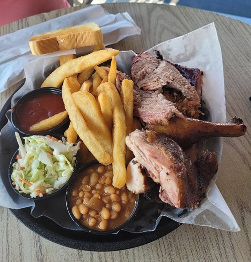 A plate of barbecue featuring smoked meat, fries, coleslaw, baked beans, and a slice of bread.