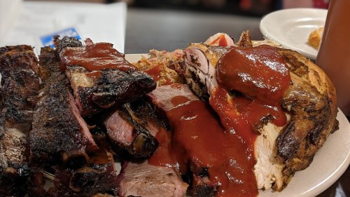 A plate of smoked ribs and pulled pork drizzled with barbecue sauce, served with a side of coleslaw.