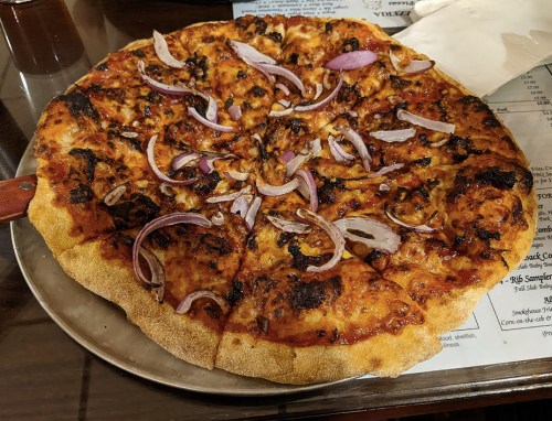 A freshly baked pizza topped with cheese, red onions, and a crispy crust, served on a metal tray.