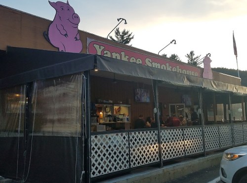 Exterior of Yankee Smokehouse restaurant with a pink pig sign and outdoor seating area.
