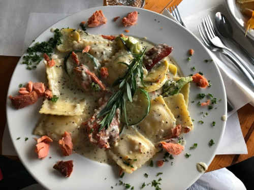 A plate of ravioli topped with herbs, smoked salmon, and a creamy sauce, garnished with parsley.