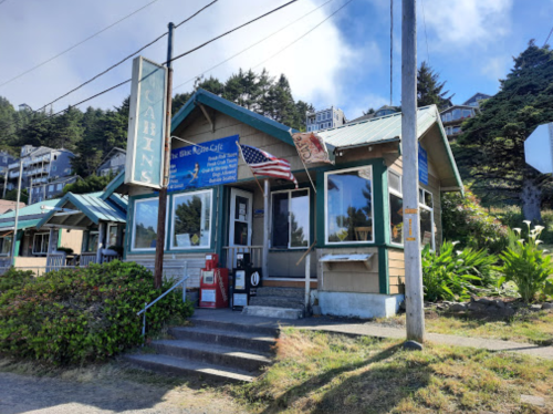 A cozy cabin-style building with a sign for a cafe, surrounded by greenery and a clear blue sky.
