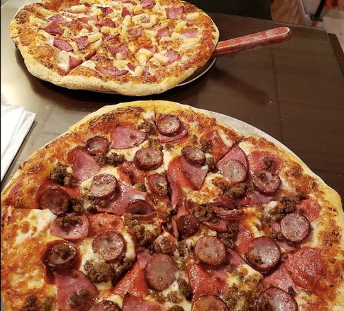 Two pizzas on a table: one topped with pepperoni and sausage, the other with ham and pineapple.