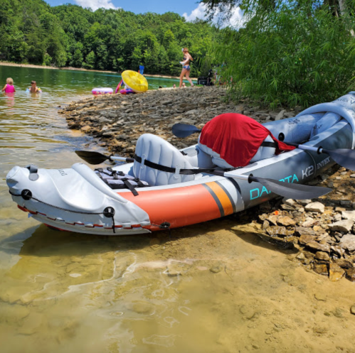 A kayak on the shore of a river, with people swimming and relaxing in the background on a sunny day.
