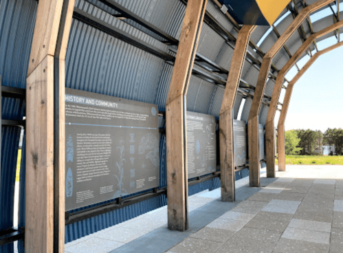 Interior view of a modern structure featuring informational panels about history and community, with wooden beams and a scenic backdrop.