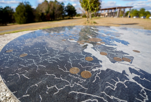 A close-up of a metallic map with coins placed on it, set in a natural outdoor environment.