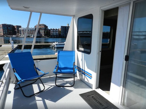 Two blue chairs on a boat deck overlooking a marina with buildings in the background and a clear blue sky.