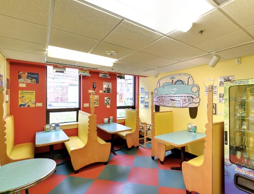 Colorful diner interior with yellow and red walls, retro car mural, and booths with blue seats.