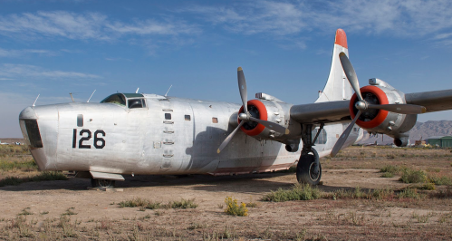 An old silver aircraft with red propellers and the number 126, resting on a dry, grassy landscape under a blue sky.
