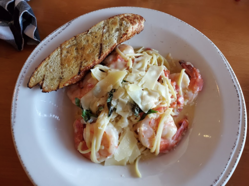 A plate of shrimp pasta with fettuccine, topped with cheese and herbs, served with a slice of toasted bread.