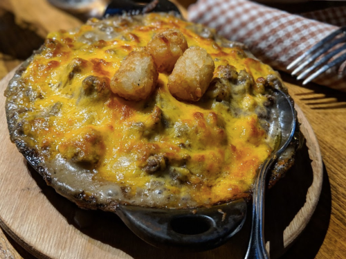 A cheesy, baked dish with ground meat and crispy tater tots on top, served in a cast iron skillet.