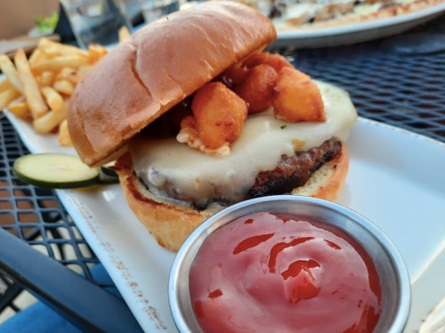 A juicy burger with melted cheese, topped with crispy bites, served with fries and a side of ketchup on a plate.