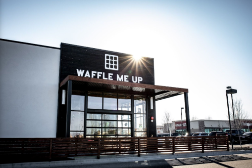 Exterior of a restaurant named "Waffle Me Up," featuring a modern design and bright sunlight in the background.