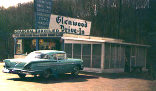 A vintage turquoise car parked in front of the Glenwood Drive-In, featuring a retro sign and a small food stand.
