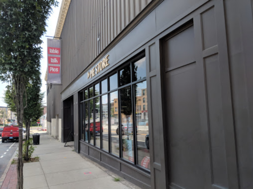 Exterior view of a store with large windows, featuring a sign that reads "Pie Store" and nearby trees along the sidewalk.