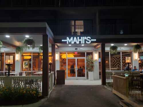 Exterior view of Mahi's restaurant at night, featuring a lit sign and outdoor seating with plants and flowers.