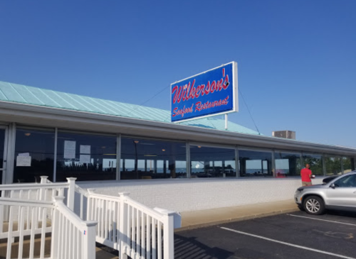 Exterior of Wilkerson's Seafood Restaurant, featuring a blue sign and a clear sky, with a parking lot in front.