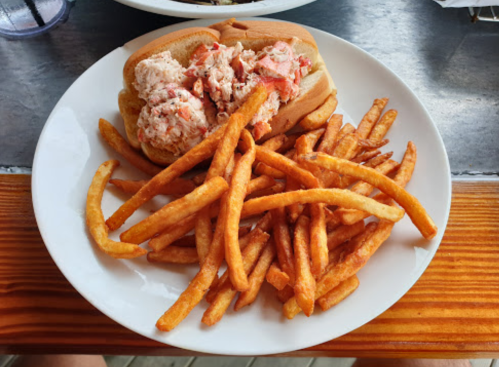 A plate with a lobster roll filled with lobster meat and a side of crispy French fries.