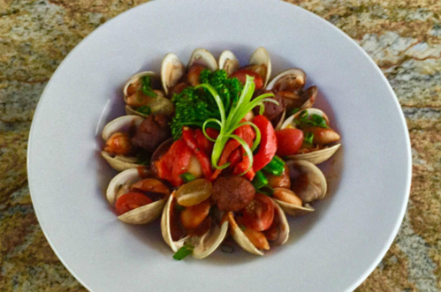 A plate of clams garnished with tomatoes, herbs, and a sprig of green, served on a textured granite surface.