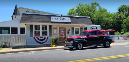 A vintage black and red car parked in front of Denson's, a charming building with an "OPEN" sign and festive decor.