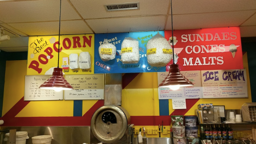 Colorful signs in a snack shop display popcorn, ice cream, and sundae options, with red pendant lights overhead.