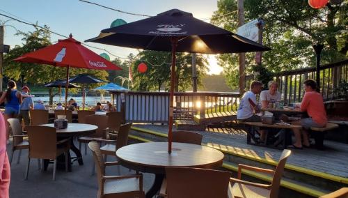 Outdoor dining area with tables, umbrellas, and people enjoying a meal by the water at sunset.