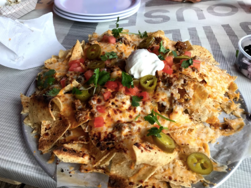 A large plate of nachos topped with cheese, jalapeños, tomatoes, cilantro, and a dollop of sour cream.