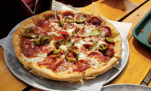 A freshly baked pepperoni pizza topped with jalapeños, served on a metal tray on a wooden table.