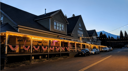 A charming building at dusk, adorned with lights and bunting, with parked cars along the road.