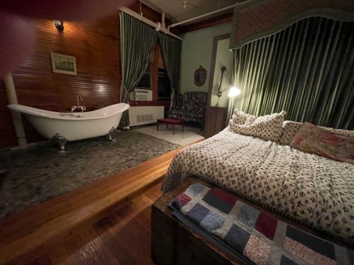 Cozy bedroom with a large bed, vintage decor, and a freestanding bathtub in a warmly lit, inviting space.