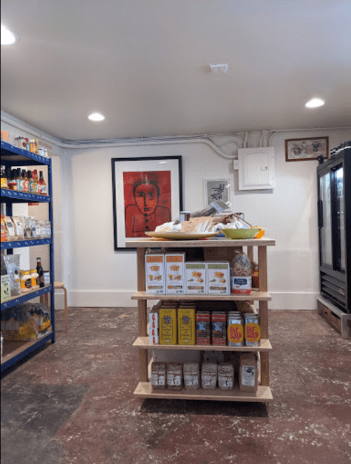 A cozy shop interior featuring shelves of products, a wooden display table, and a colorful framed artwork on the wall.